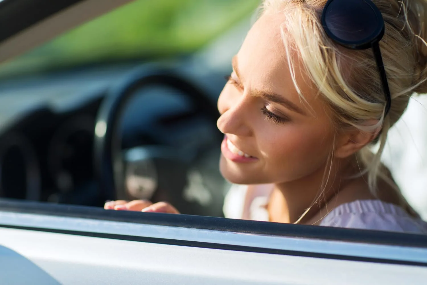 Jeune conducteur au volant d’une petite citadine d’occasion devant un garage, avec un vendeur et une clé de voiture en main.