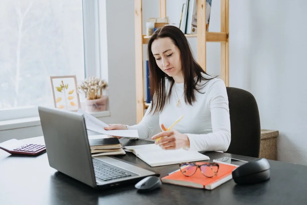 Un auto-entrepreneur utilise un ordinateur portable pour éditer une facture sur un logiciel de gestion, avec un bureau de travail épuré.