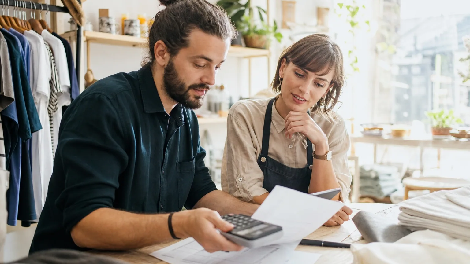 Un couple d'indépendants examine ensemble des documents administratifs et une calculatrice sur la table d'un atelier