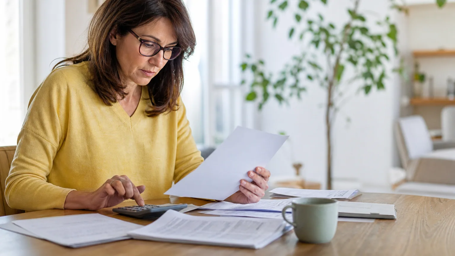 Personne assise à une table examinant des factures et relevés bancaires avec une calculatrice