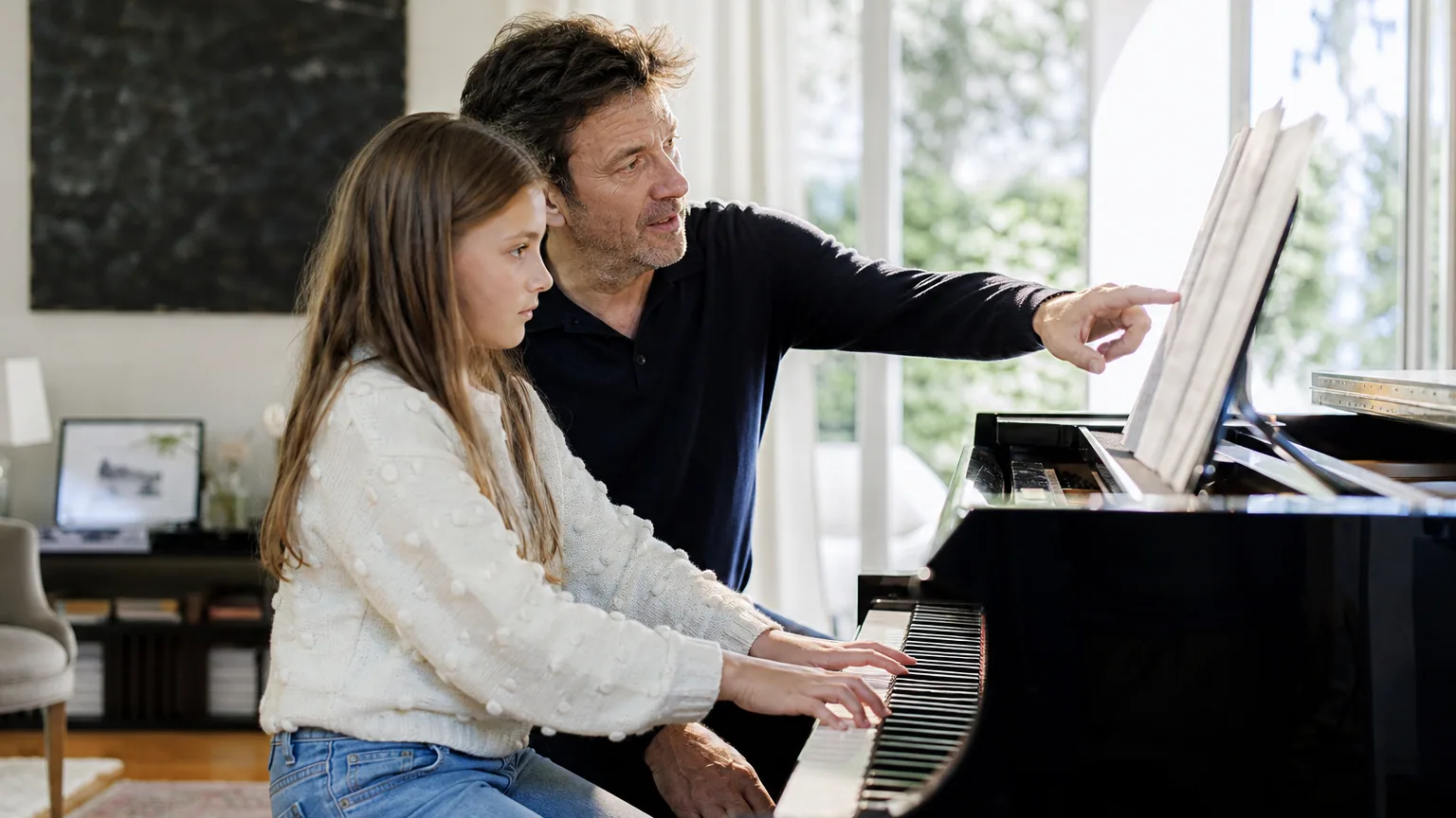 Professeur de musique donnant un cours de piano à domicile à une élève, partitions ouvertes sur le pupitre