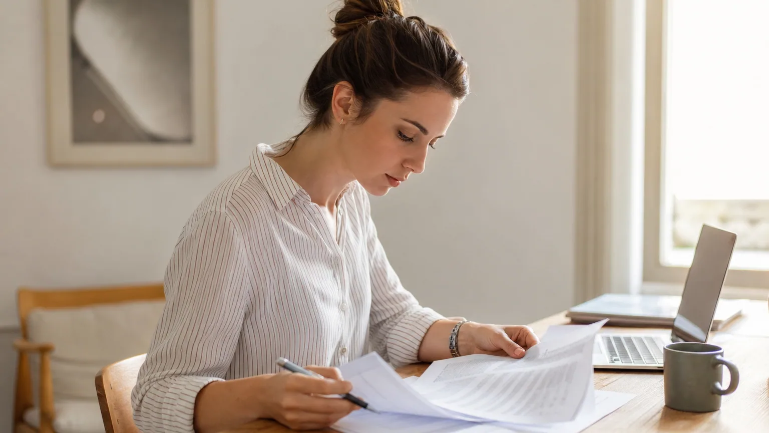 Indépendante relisant un contrat imprimé annoté au stylo sur un bureau clair avec un ordinateur portable