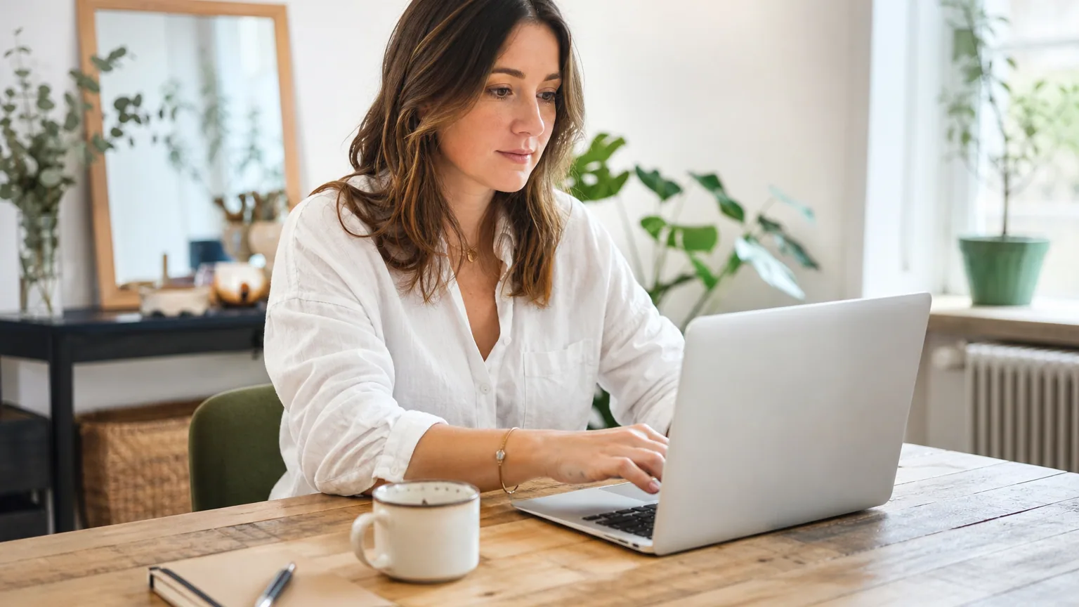 Rédactrice web indépendante tapant un article sur son ordinateur portable, tasse de café et carnet de notes sur le bureau