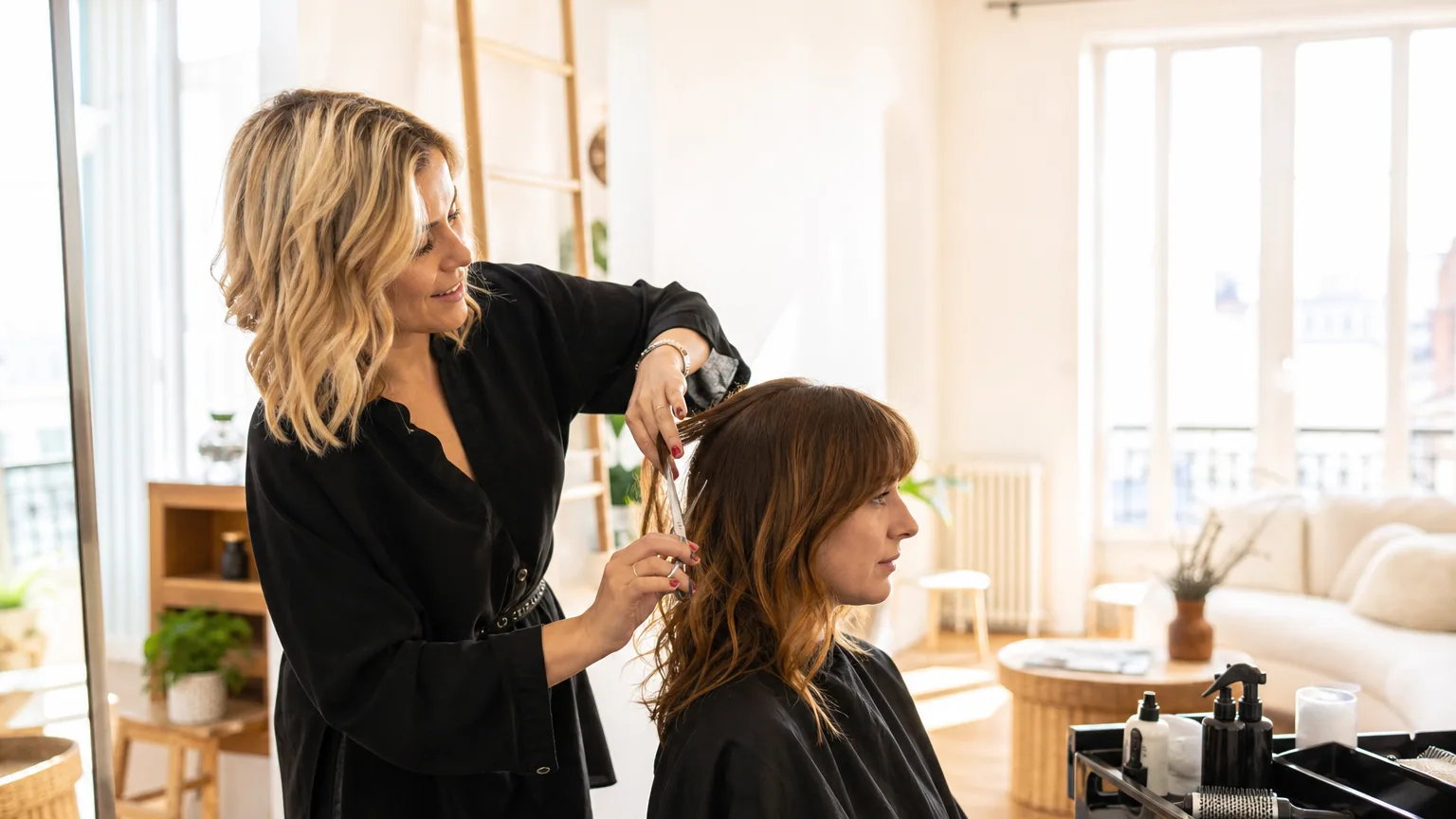 Coiffeuse indépendante réalisant une coupe de cheveux à domicile chez une cliente dans un salon lumineux