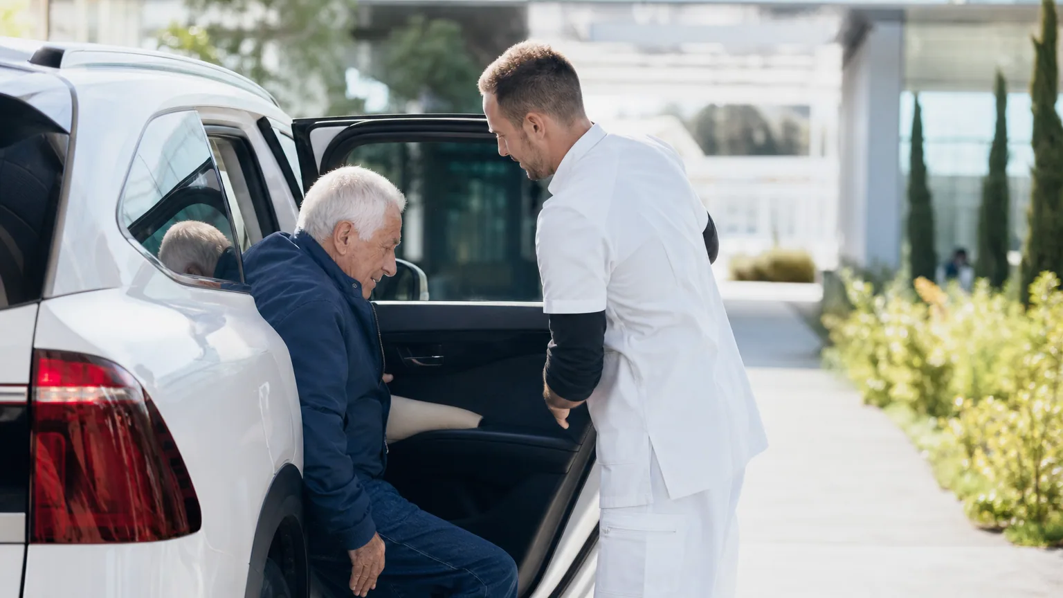 Conducteur de véhicule sanitaire léger aidant un patient à s'installer à bord devant un établissement de santé