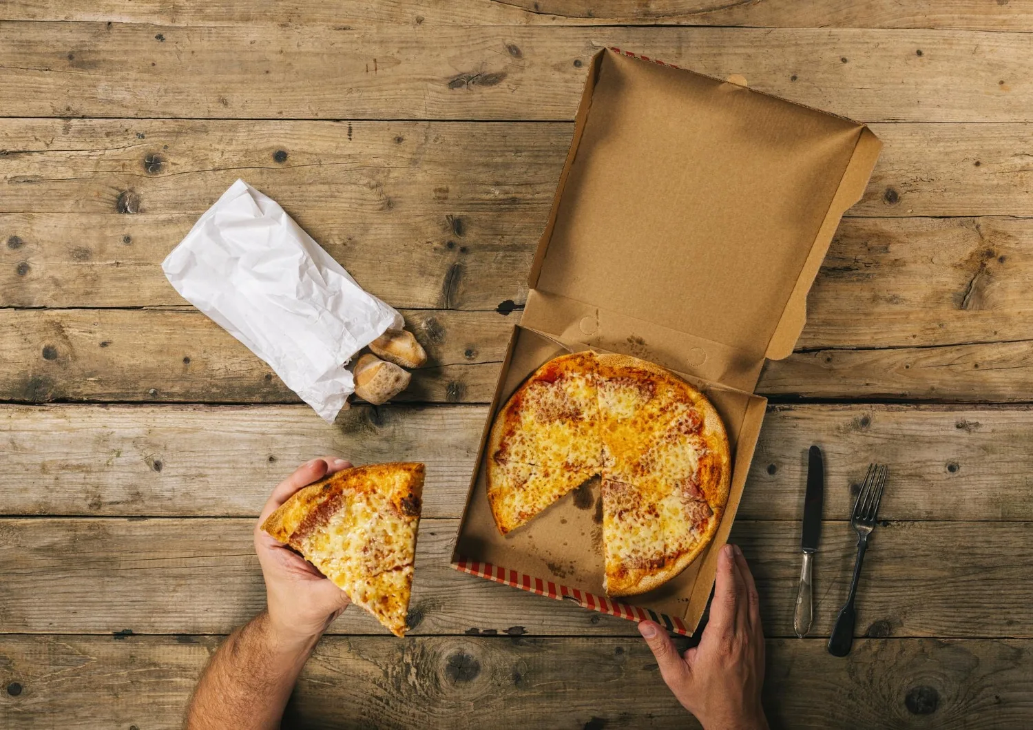 Une pizza surgelée et une boîte de livraison de pizza fraîche posées sur une table de bureau avec des ordinateurs en arrière-plan.