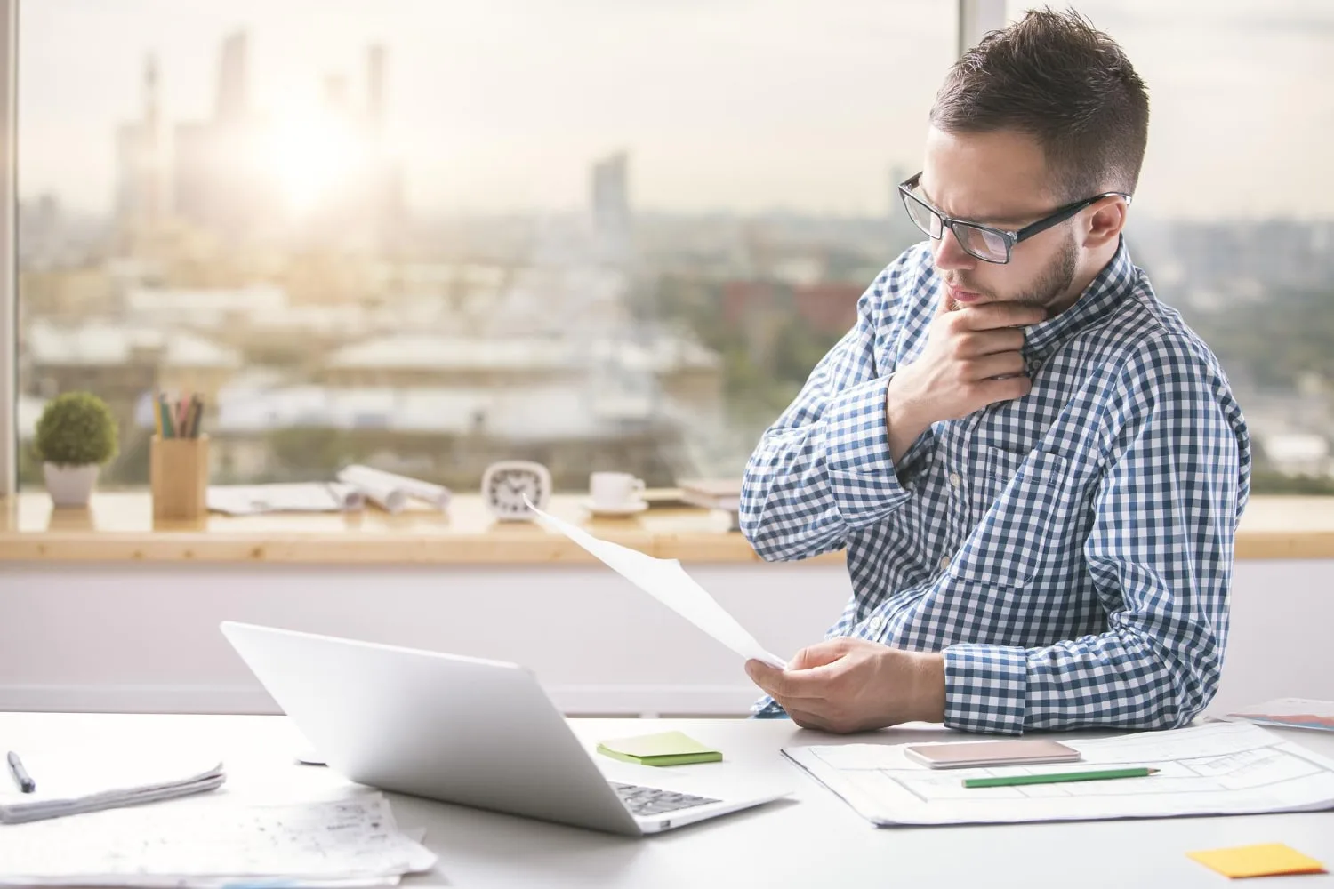 Entrepreneur vérifiant des factures impayées sur un ordinateur, avec dossier de relance et téléphone sur le bureau