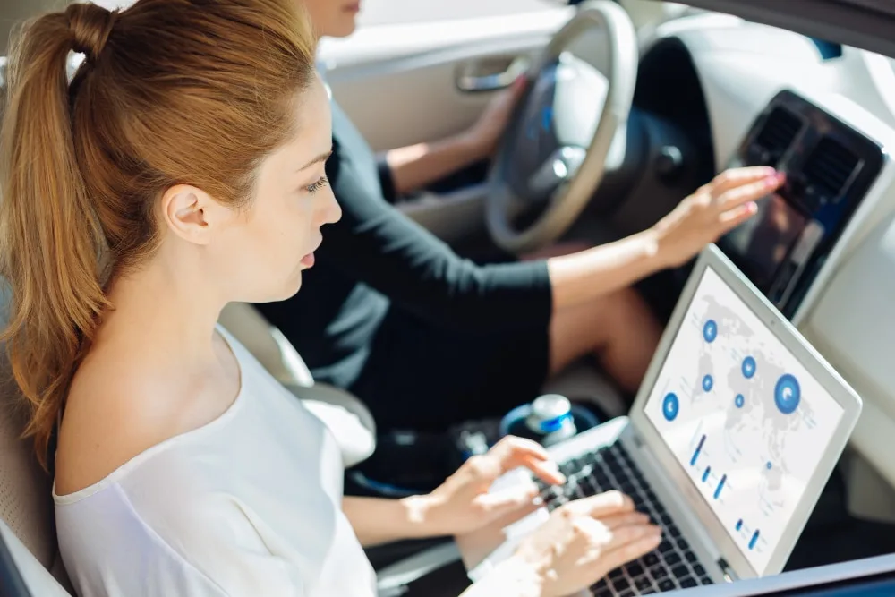 Commercial d’entreprise au volant d’une voiture de société avec un ordinateur portable et un dossier sur le siège passager